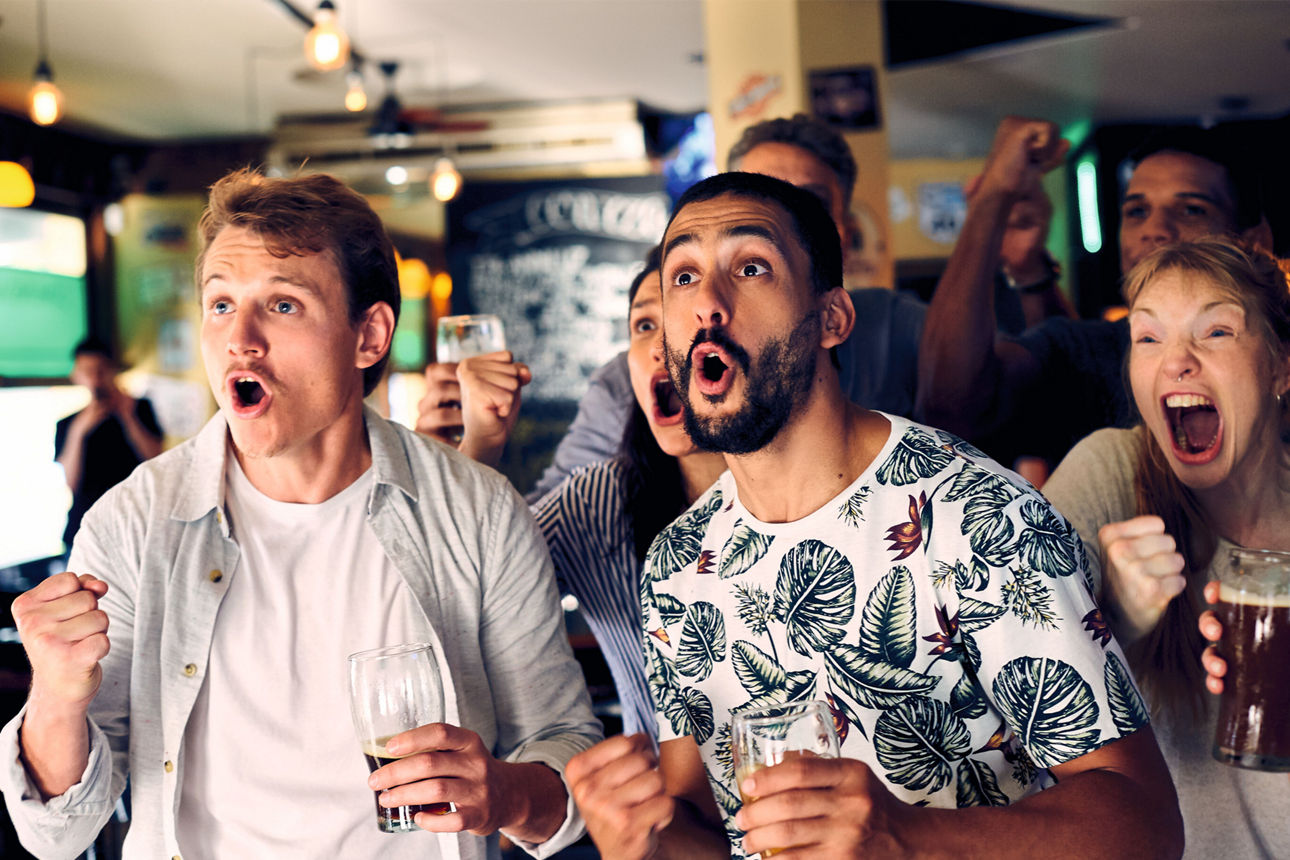 Gruppe von Personen jubelt in einer Bar und verfolgt gemeinsam ein Sportereignis.