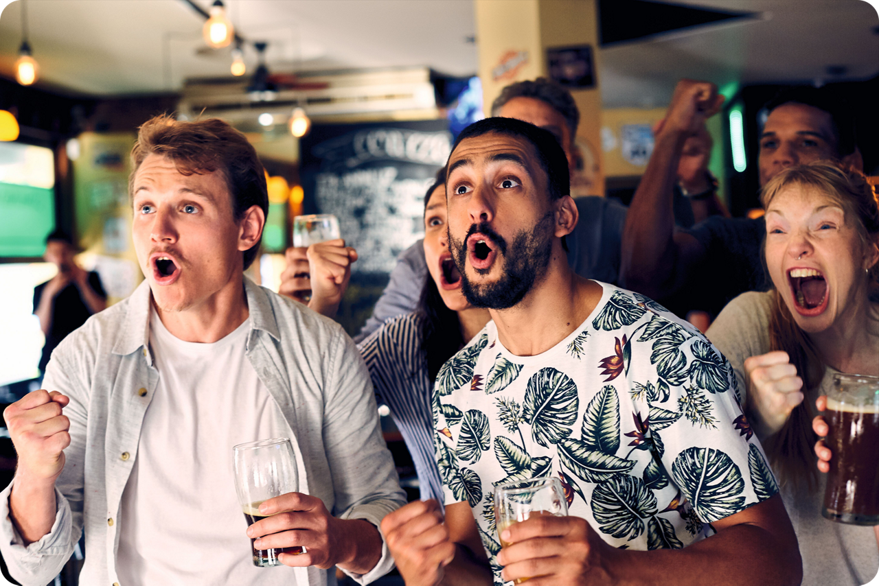 Gruppe von Personen jubelt in einer Bar und verfolgt gemeinsam ein Sportereignis.