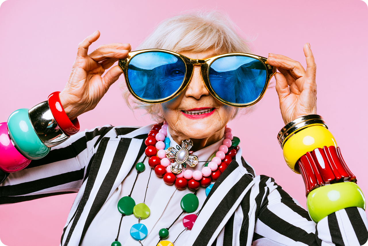 Eine ältere Dame in bunter Kleidung trägt eine sehr große Sonnenbrille