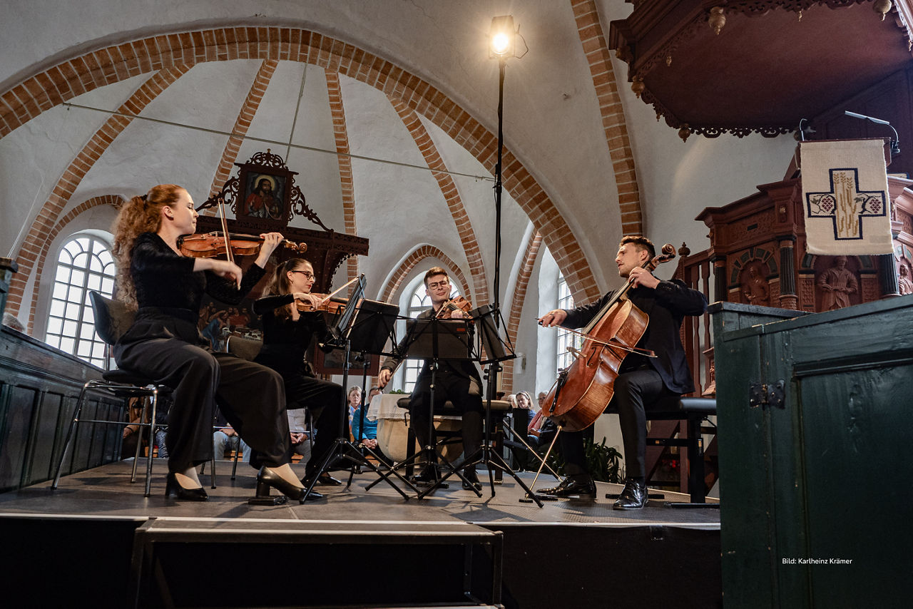 Ein Orchester spielt Insstrumente auf einer Bühne in einem Gewölbe