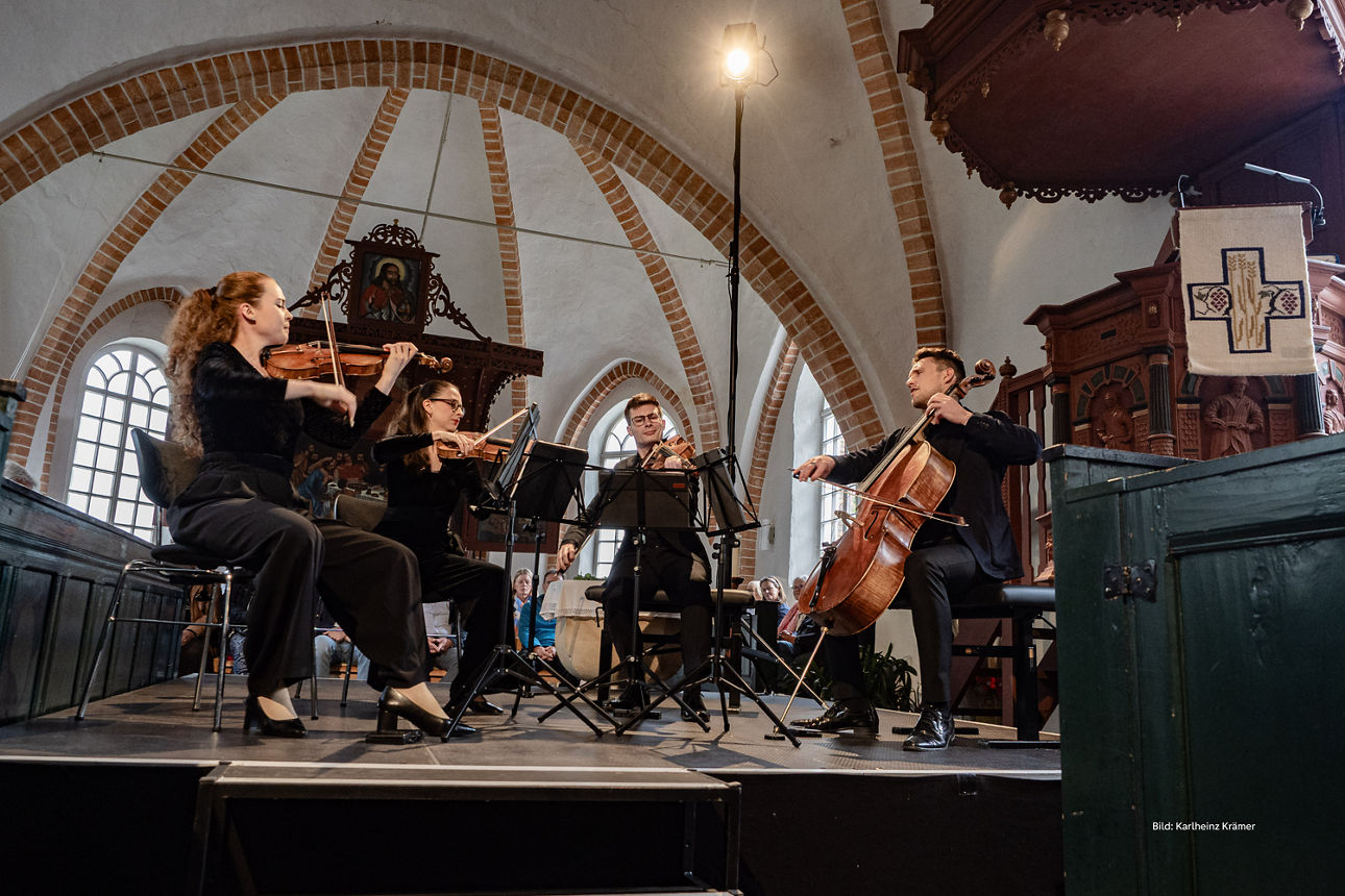Ein Streichtrio spielt in einer sonnendurchfluteten Kirche, und ihre Musik erfüllt den hallenden Raum.
