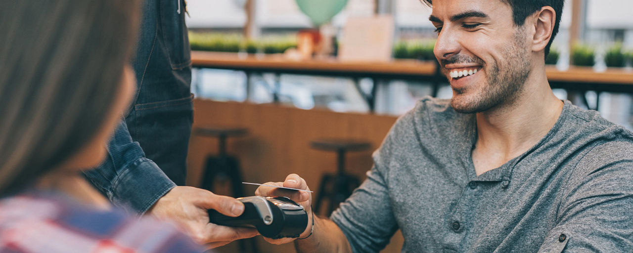 Junger Mann in einem Café beim kontaktlosen Bezahlen mit der girocard