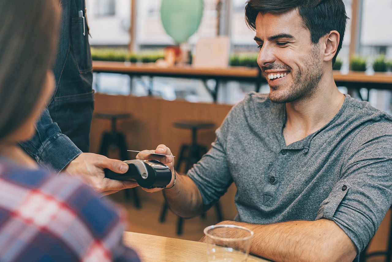 Junger Mann in einem Café beim kontaktlosen Bezahlen mit der girocard