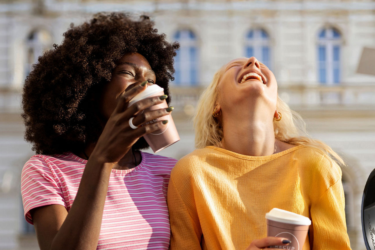 Zwei junge lachende Frauen mit einem Coffee-to-go