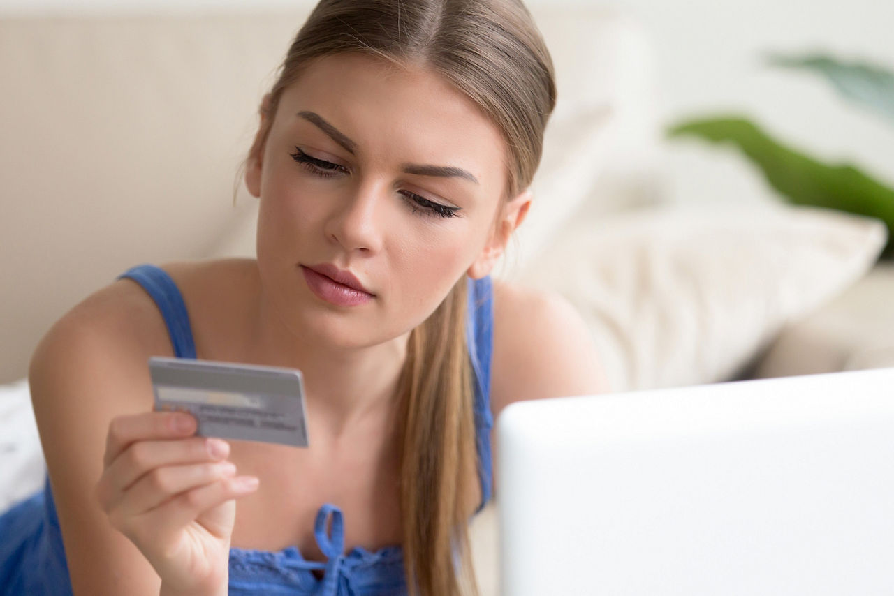 Junge Frau sizt auf dem Sofa und schaut auf ihre girocard