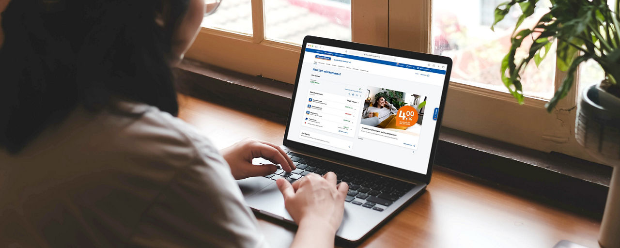 Frau sitzt in der Küche und erledigt im Online-Banking ihre Finanzen