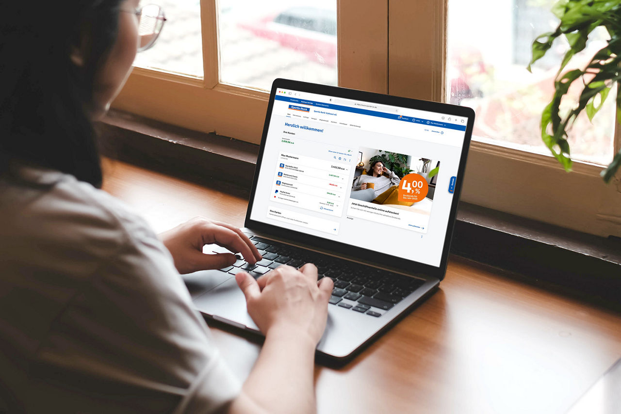 Frau sitzt in der Küche und erledigt im Online-Banking ihre Finanzen