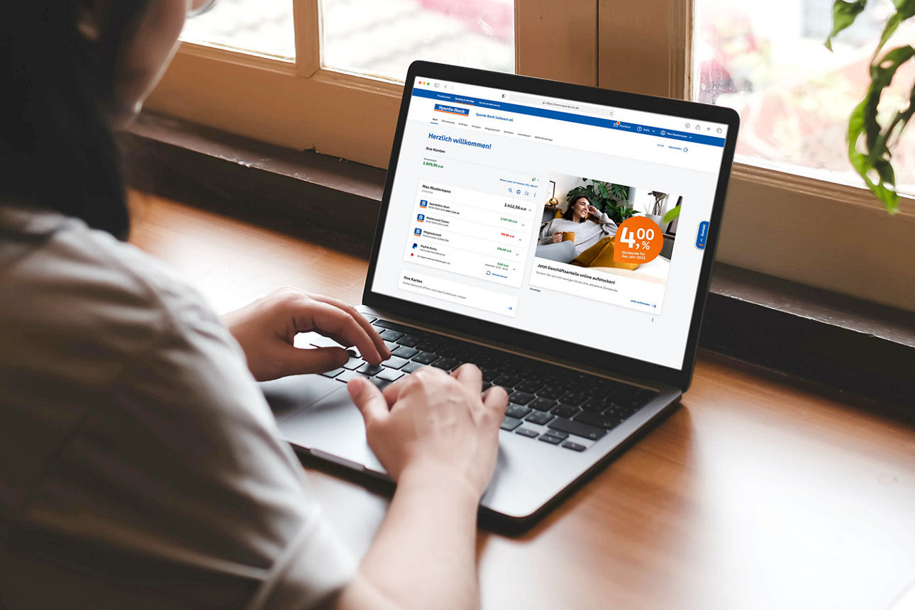 Frau sitzt in der Küche und erledigt im Online-Banking ihre Finanzen