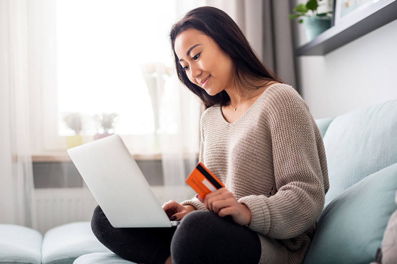 Junge Frau mit Laptop und Bankkarte auf der Couch