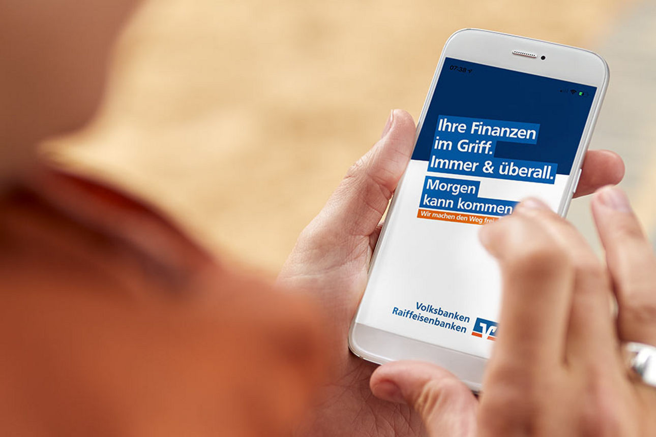 Person hat Handy mit Volksbank Slogan auf dem Display in der Hand Person hat Handy mit Volksbank Slogan auf dem Display in der Hand