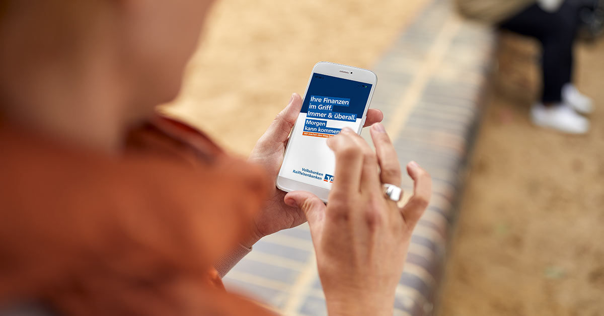 Zwei Hände halten ein Smartphone mit geöffneter Volksbanken-Raiffeisenbanken-Seite