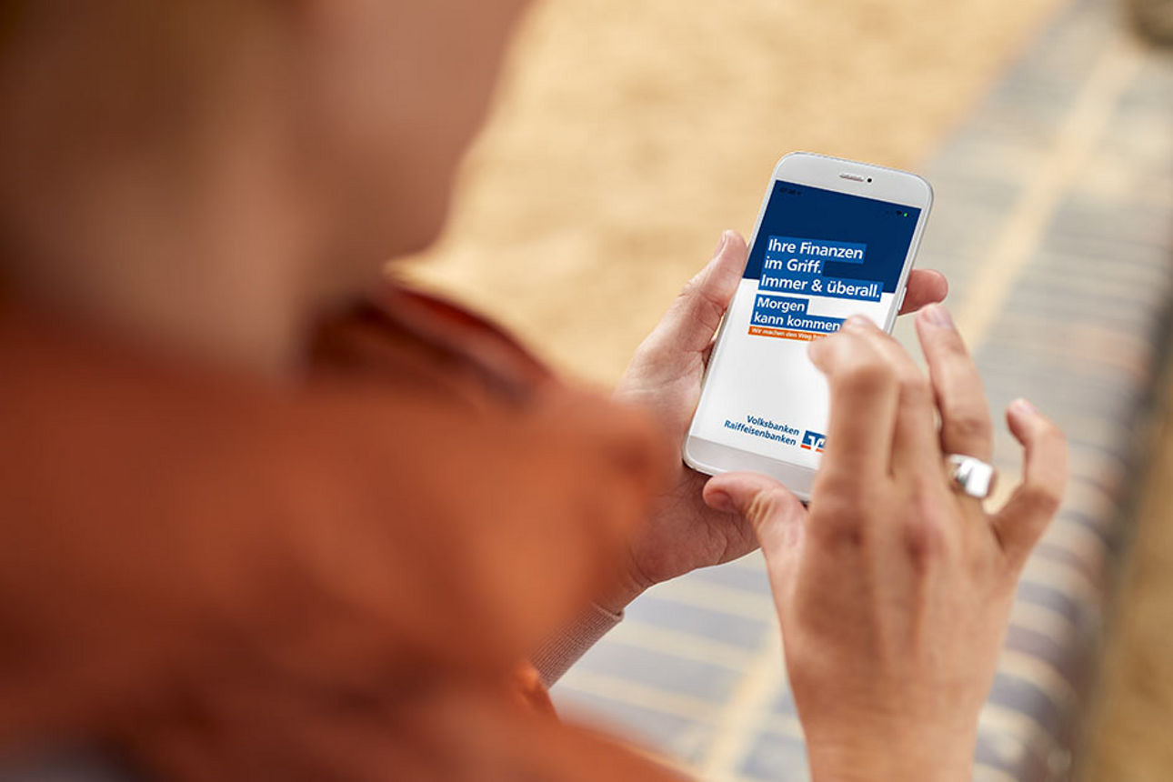 Zwei Hände halten ein Smartphone mit geöffneter Volksbanken-Raiffeisenbanken-Seite