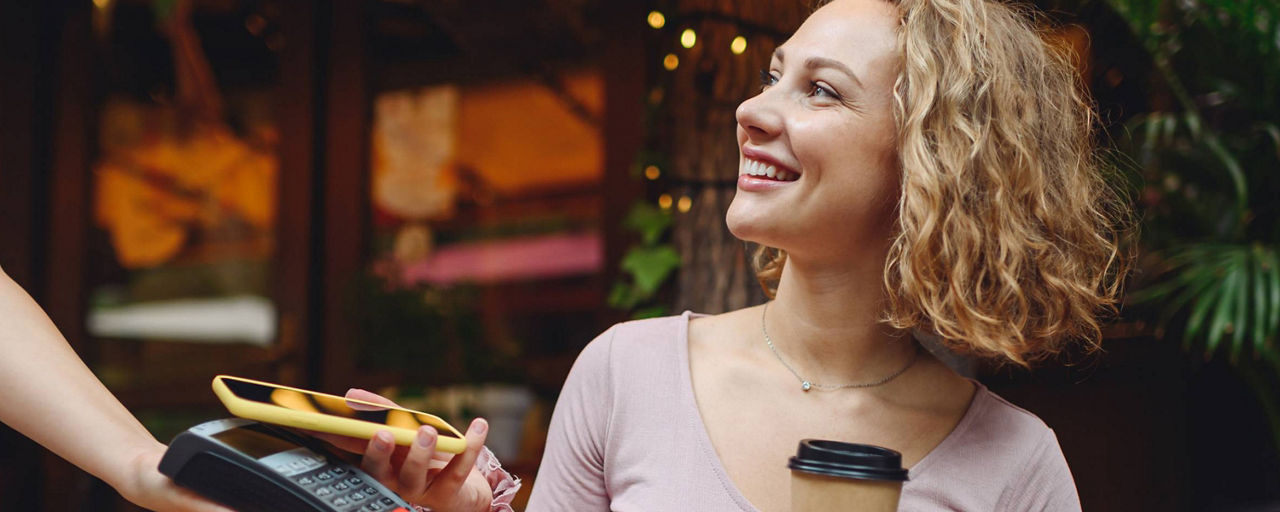 Frau bezahlt ihren Kaffee in einem Restaurant mit ihrem Handy am Kartenlesegerät