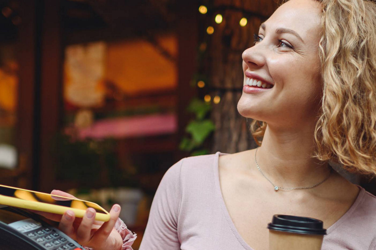 Frau bezahlt ihren Kaffee in einem Restaurant mit ihrem Handy am Kartenlesegerät