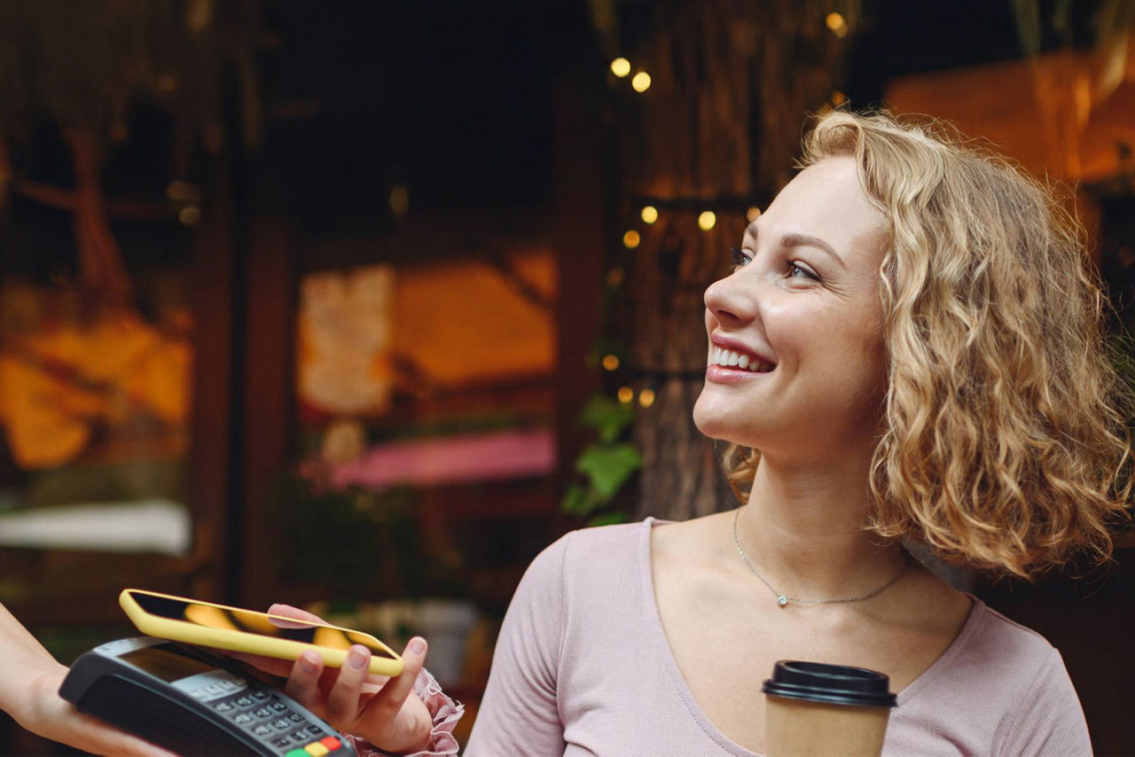 Junge Frau bezahlt mit ihrem Handy einen Kaffee