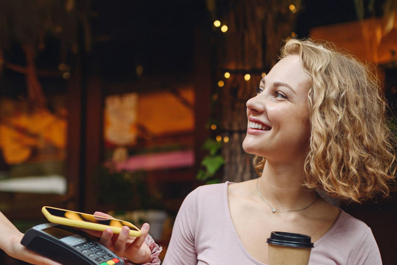 Junge Frau bezahlt mit ihrem Handy einen Kaffee