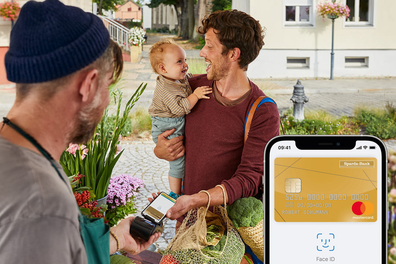 Mann mit Kind auf dem Arm bezahlt auf dem Markt seinen Einkauf per Apple Pay