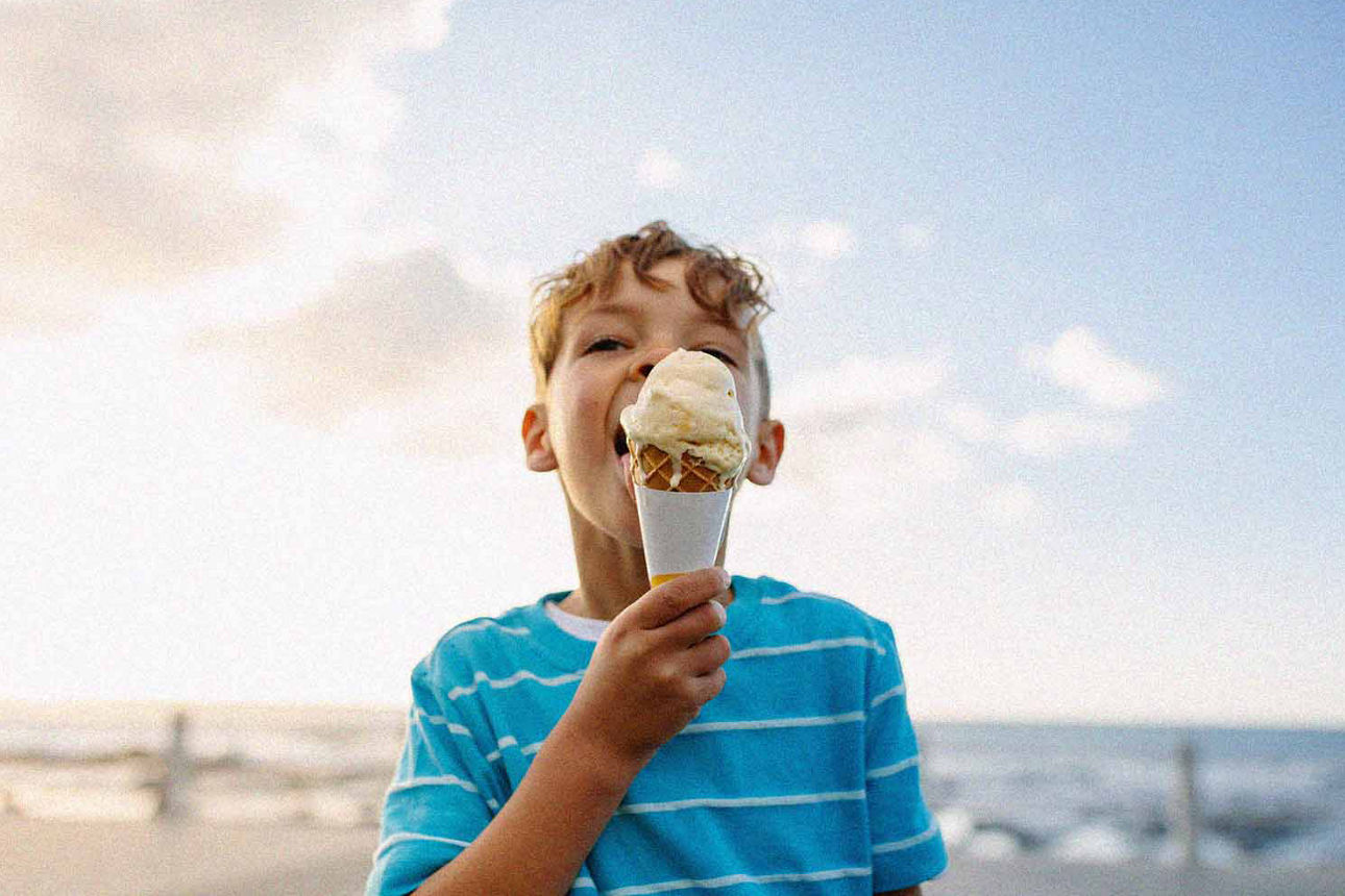 Kleiner Junge schleckt fröhlich sein Eis am Strand