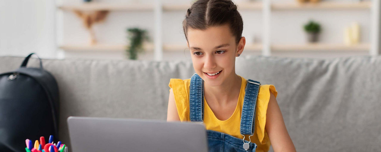 Mädchen sitzt vor dem Laptop und erledigt ihre Hausaufgaben