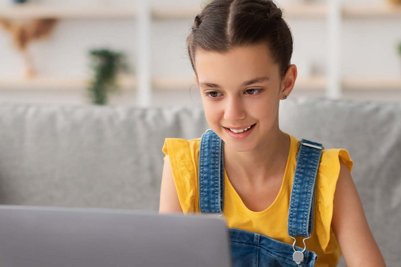 Mädchen sitzt vor dem Laptop und erledigt ihre Hausaufgaben