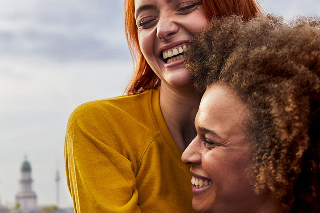 Zwei Frauen umarmen sich lächelnd auf einer Dachterrasse