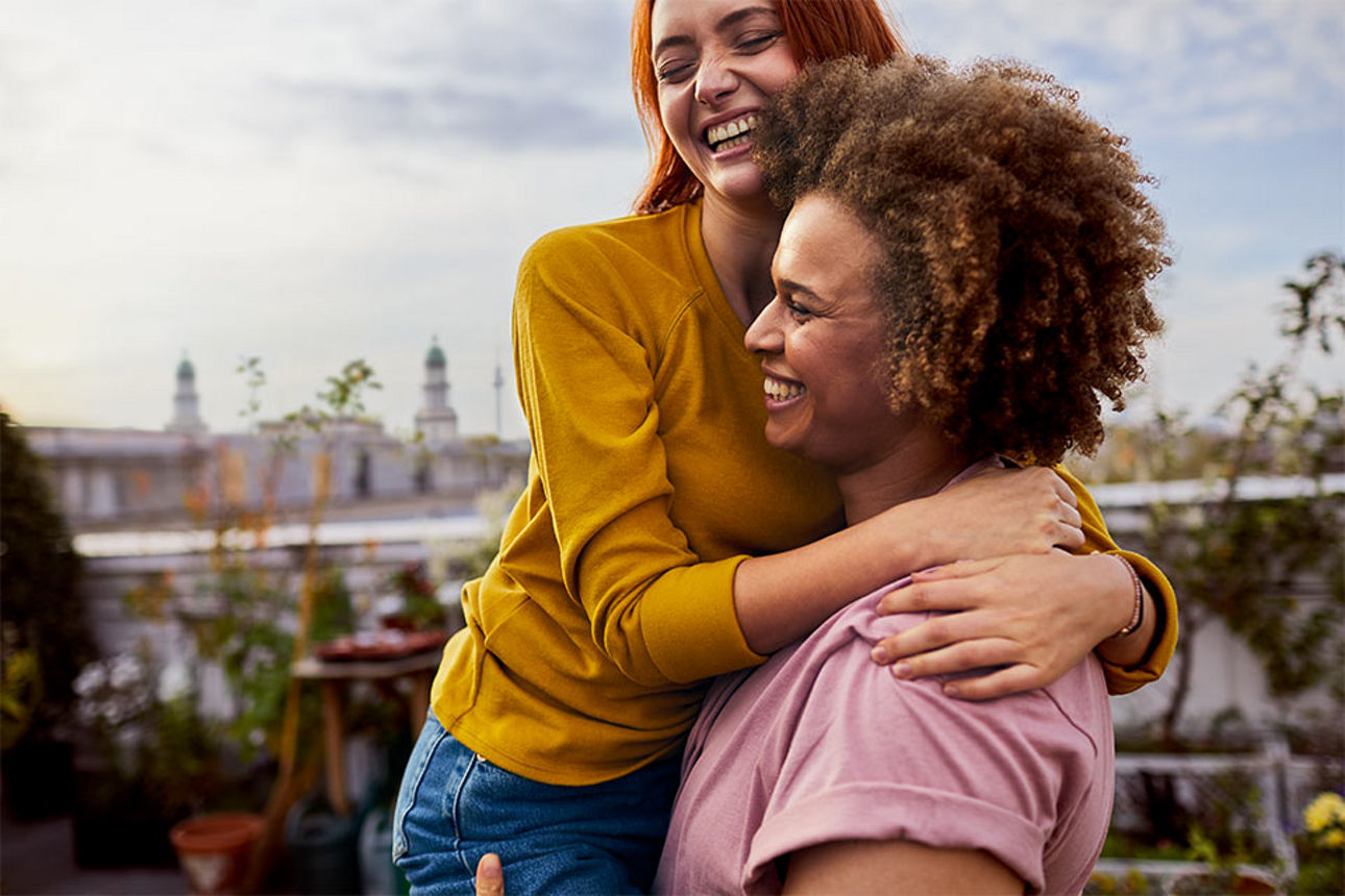 Zwei Frauen umarmen sich lächelnd auf einer Dachterrasse