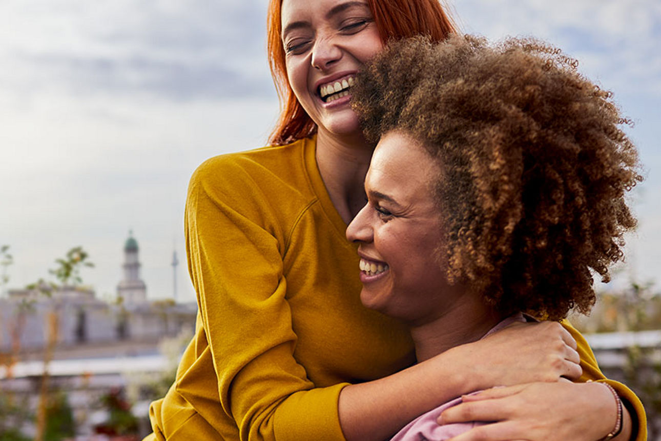 Zwei Frauen umarmen sich lächend auf einer Dachterrasse