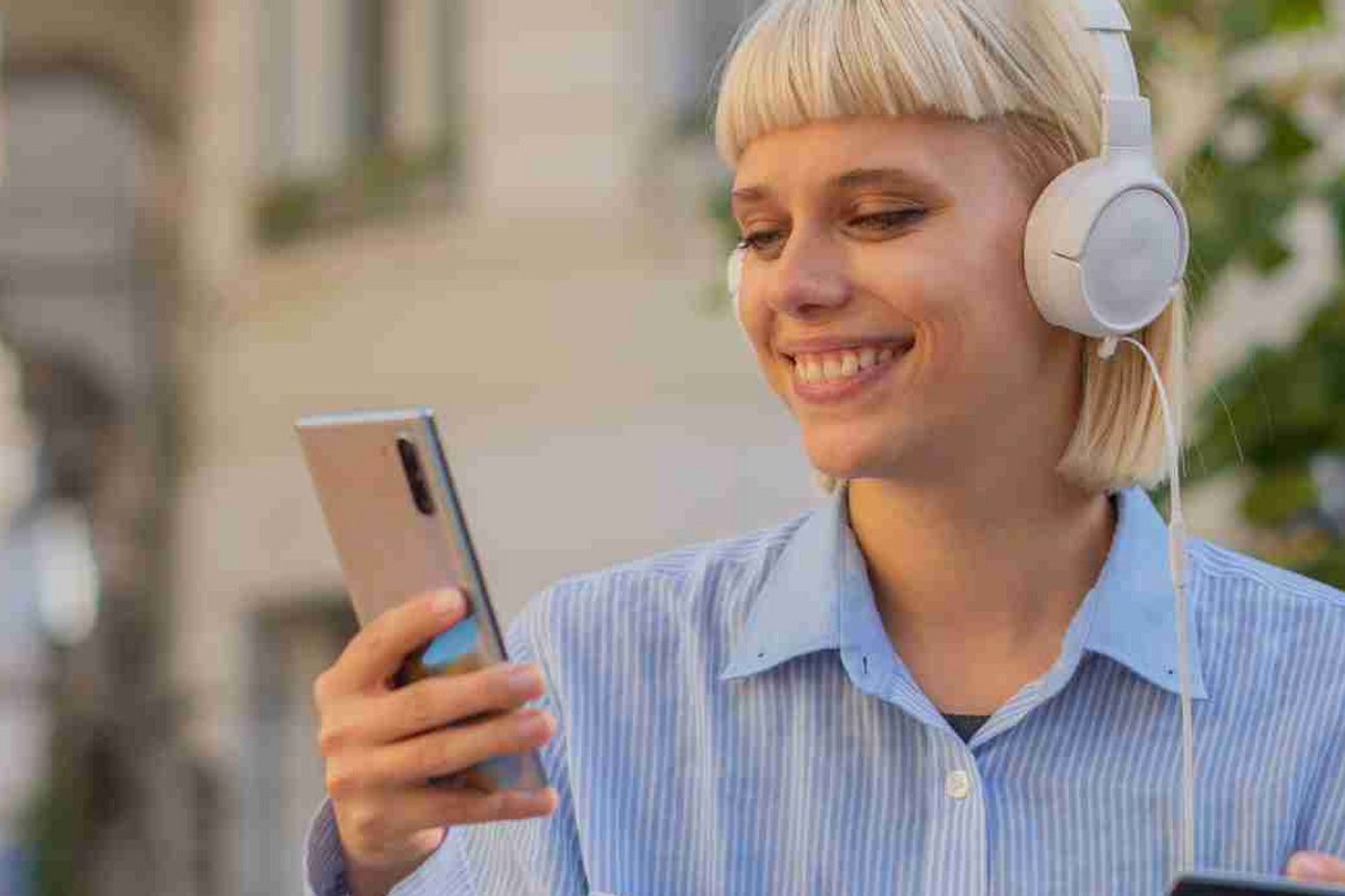 Junge Frau mit Kopfhörern hält ein Smartphone und eine Bankkarte in der Hand 