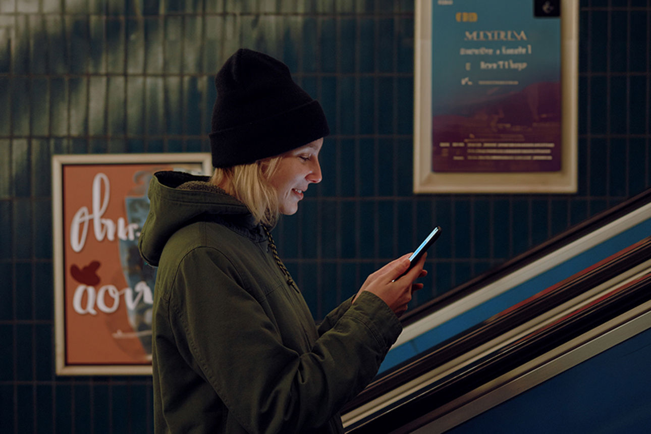 Frau auf einer Rolltreppe mit einem Handy in der Hand.