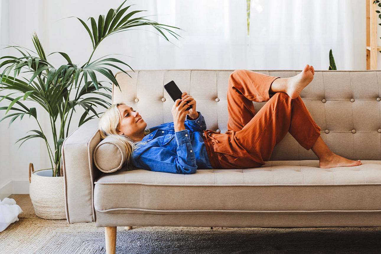 Frau liegt entspannt auf dem Sofa und nutzt ihr Smartphone.