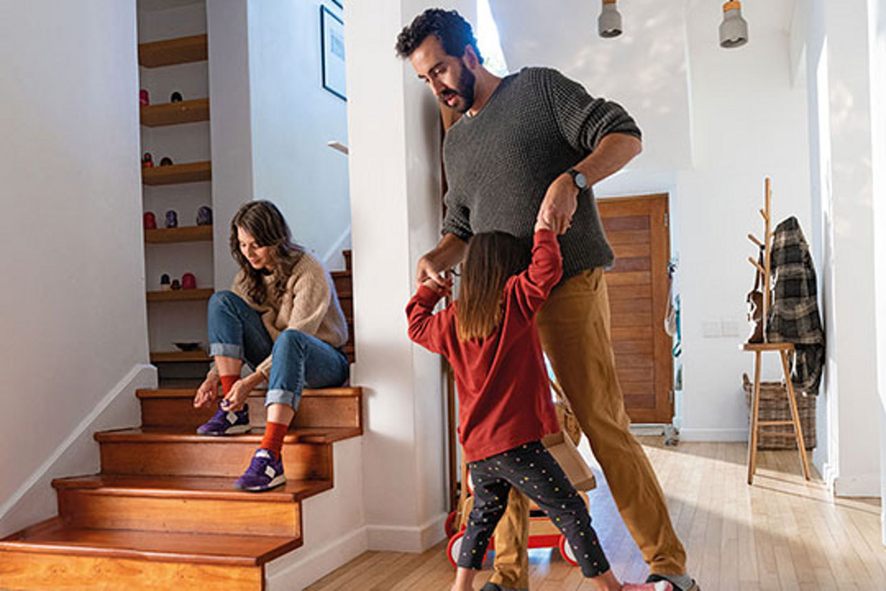 Junge Familie in Ihrem Hausflur. Der Papa albert mit der Tochter, die Mutter zieht sich Schuhe an.