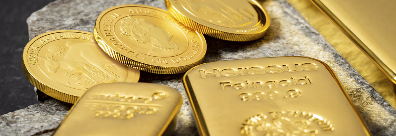 Es liegen drei Gold Münzen und zwei Goldbarren auf einem Stein