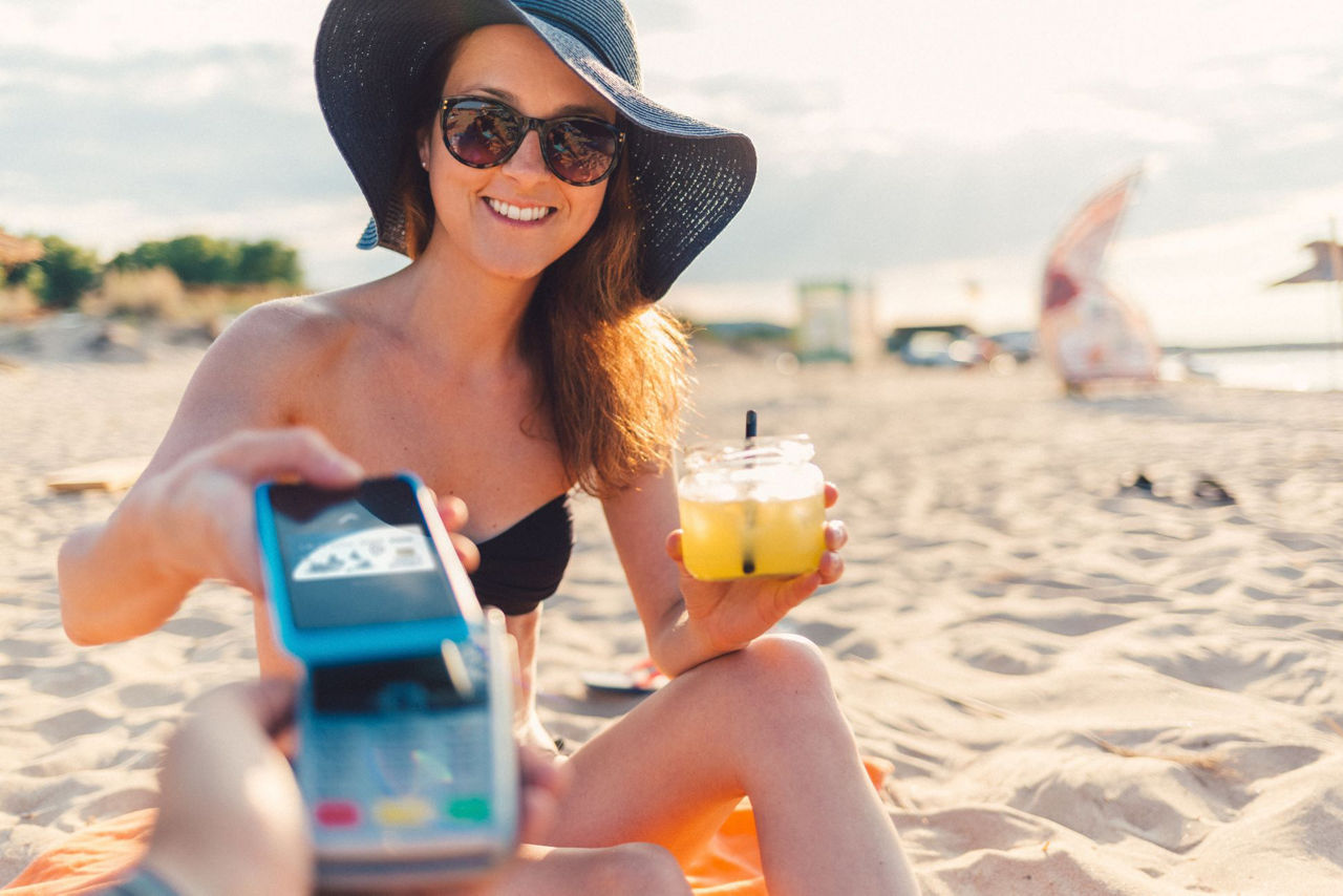 goldcard-kreditkarte-gold-mastercard-volksbank-raiffeisenbank-eg-frau-am-strand-zahlt-cocktail