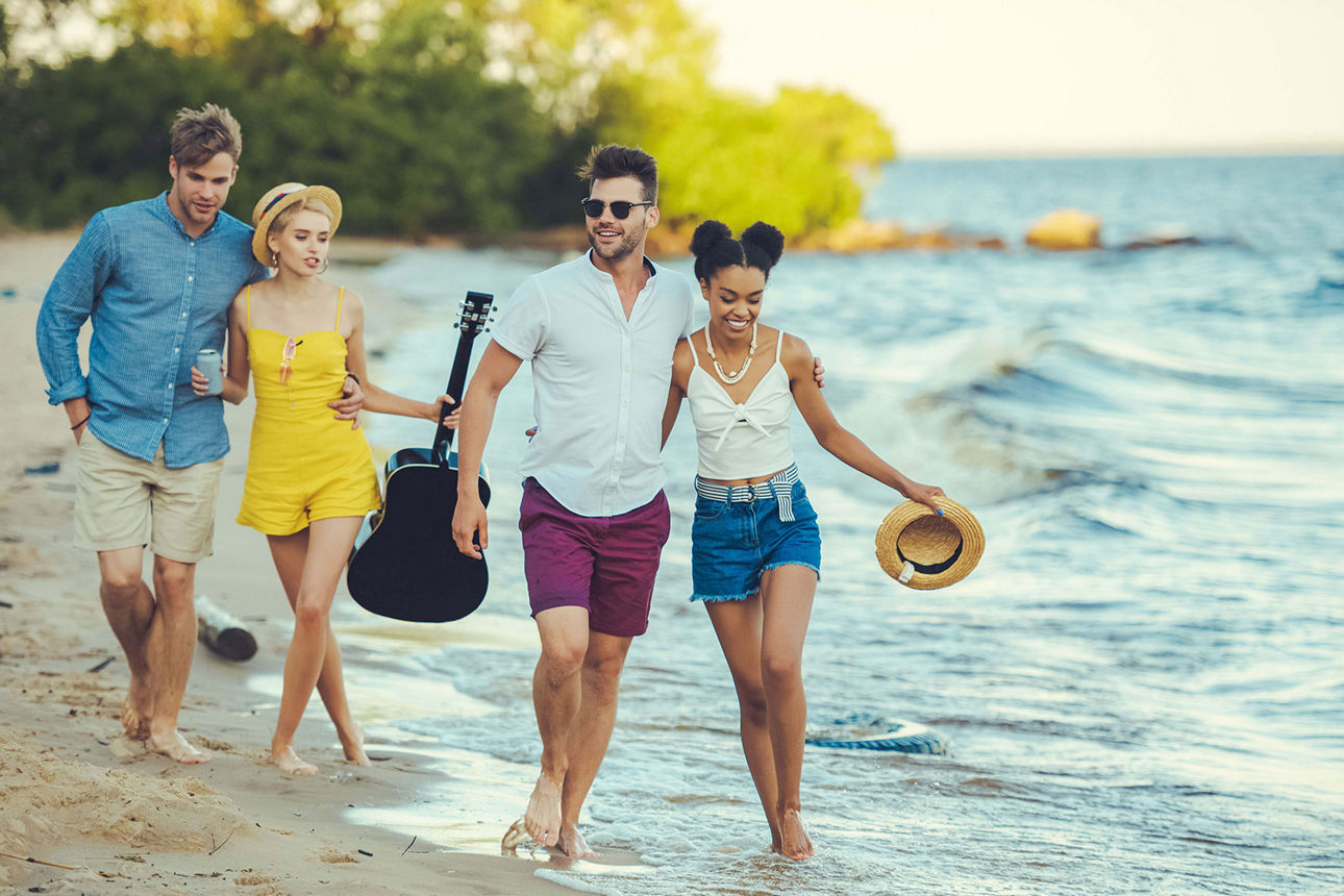 Zwei junge Paare gehn an einem Sandstrand spazieren
