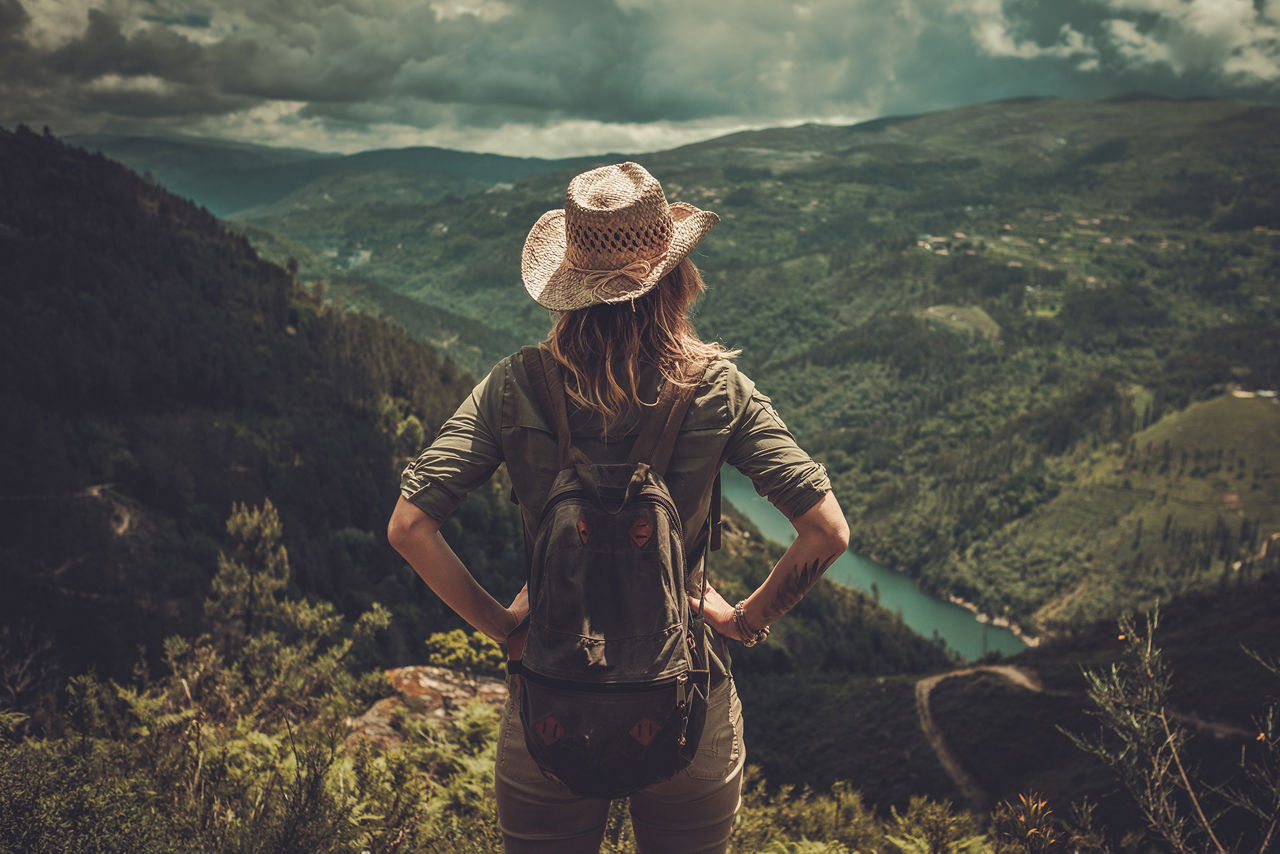 Wanderin stemmt die Hände in die Hüften und blickt von einem Berg auf ein grünes Tal