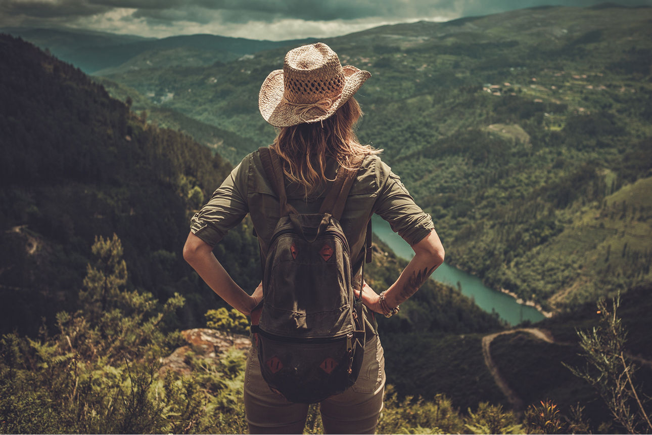 Wanderin stemmt die Hände in die Hüften und blickt von einem Berg auf ein grünes Tal