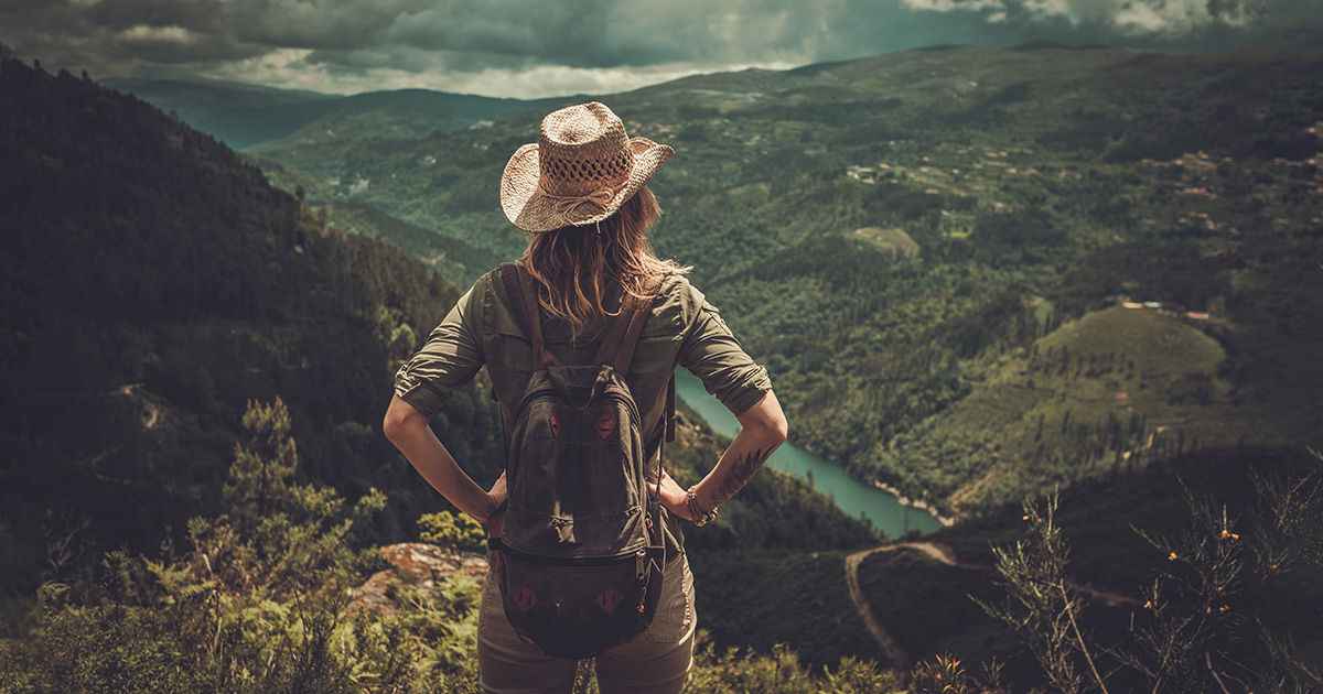 Frau mit Sonnenhut steht an Berg und schaut ins Tal.