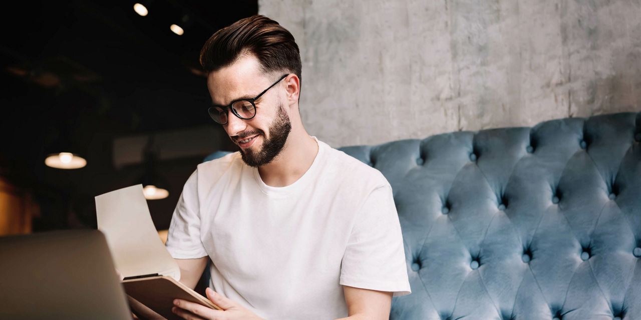 Mann sitzt mit einem Block vor einem Laptop