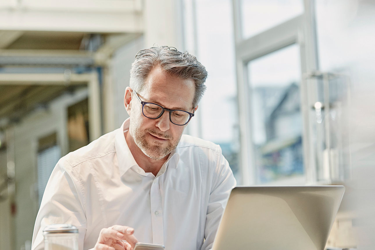 Mann sitzt am Laptop mit Smartphone