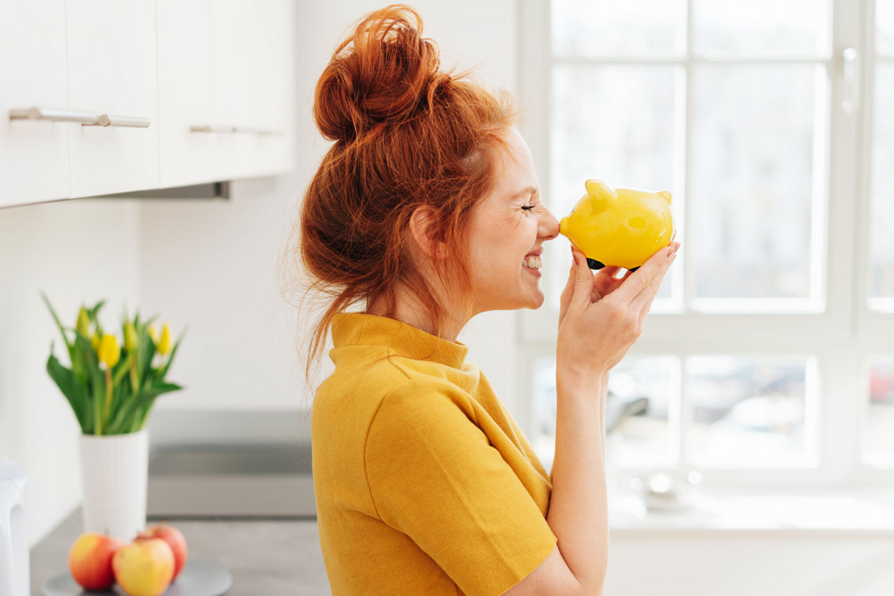 Frau mit roten Haaren freut sich über ein Sparschwein
