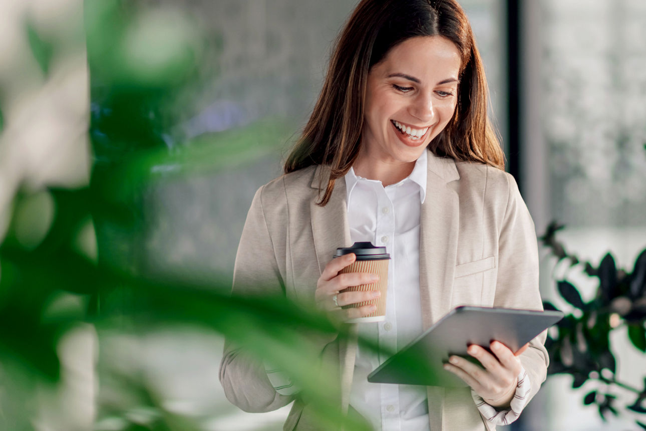 Frau mit Kaffeebecher schaut auf ein Tablet