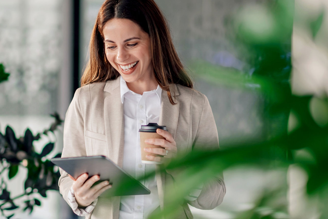Frau mit Kaffeebecher schaut auf ein Tablet