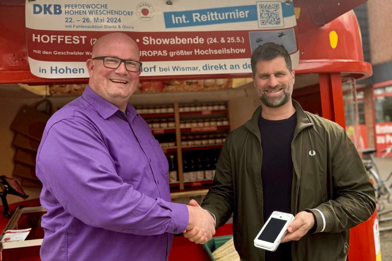 Zwei Männer stehen händeschüttelnd vor einem Erdbeerstand.