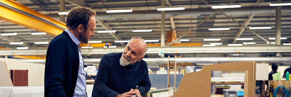 Zwei Männer stehen in einer großen, industriellen Lagerhalle und unterhalten sich.