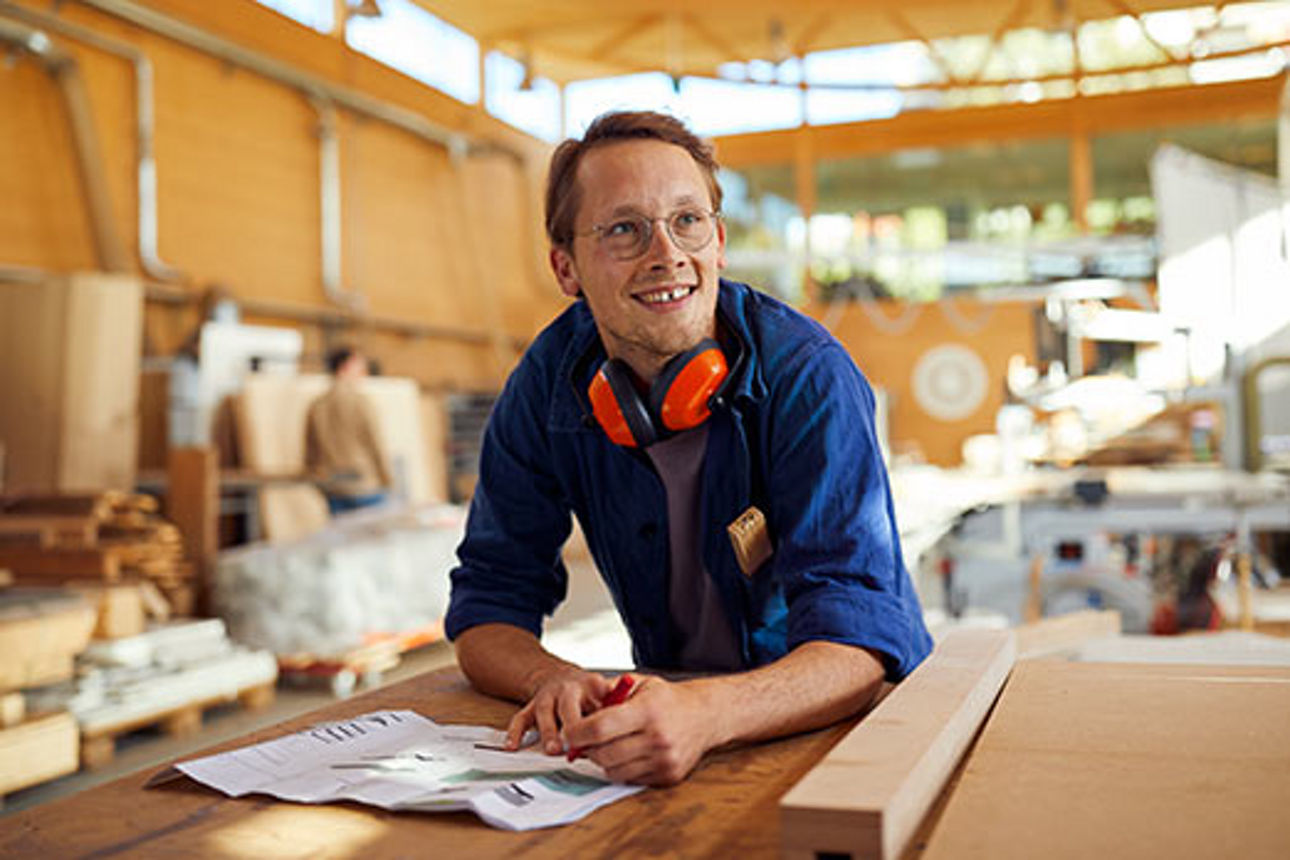 Junger Mitarbeiter mit Stift und Produktionsplan in einer Fabrikhalle