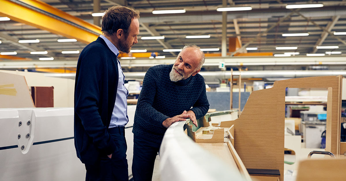 Zwei Männer stehen in einer Produktionshalle und schauen sich an.