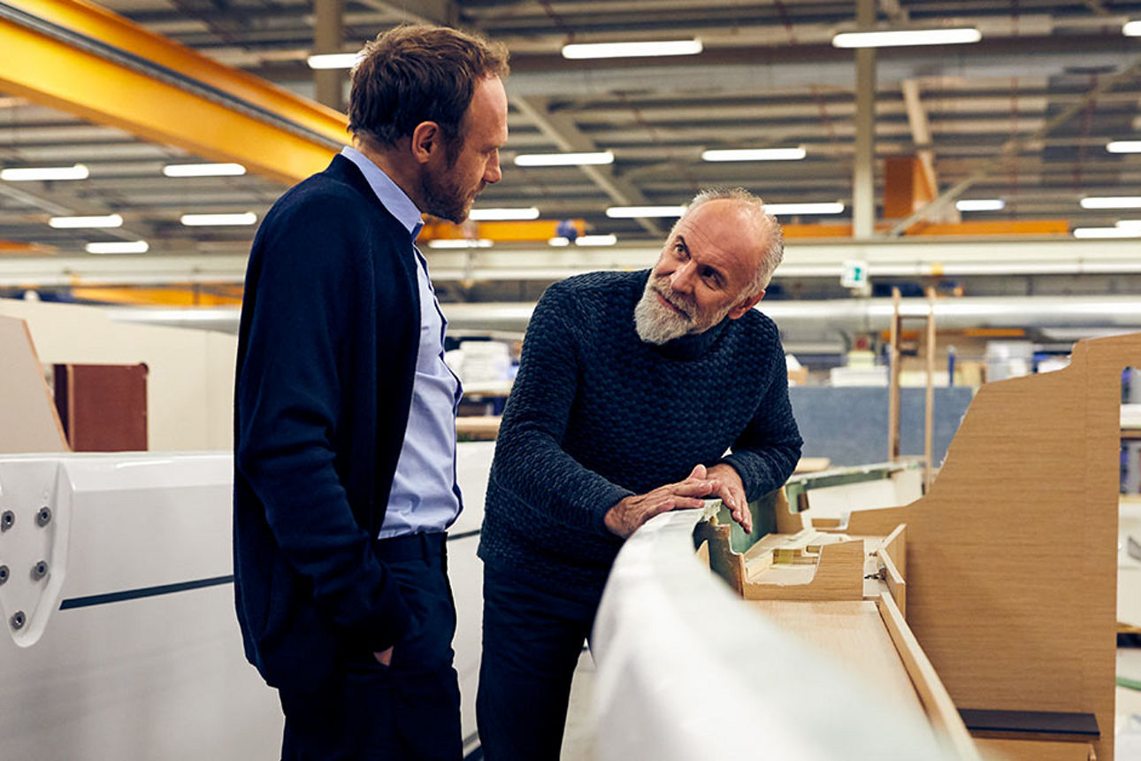 Zwei Männer stehen in einer Produktionshalle und schauen sich an.