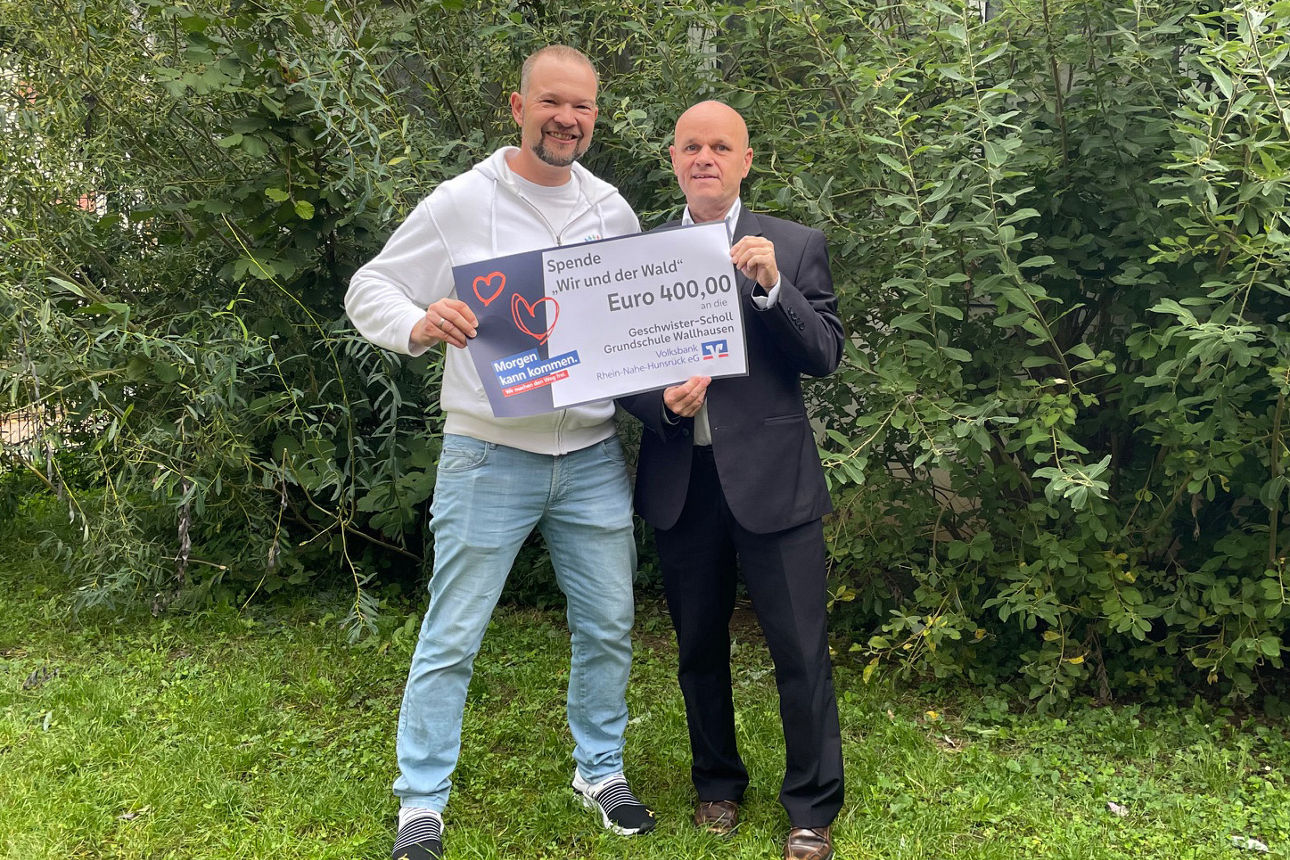 Zwei Erwachsene stehen auf einer Wiese und halten einen Spendenscheck in der Hand.