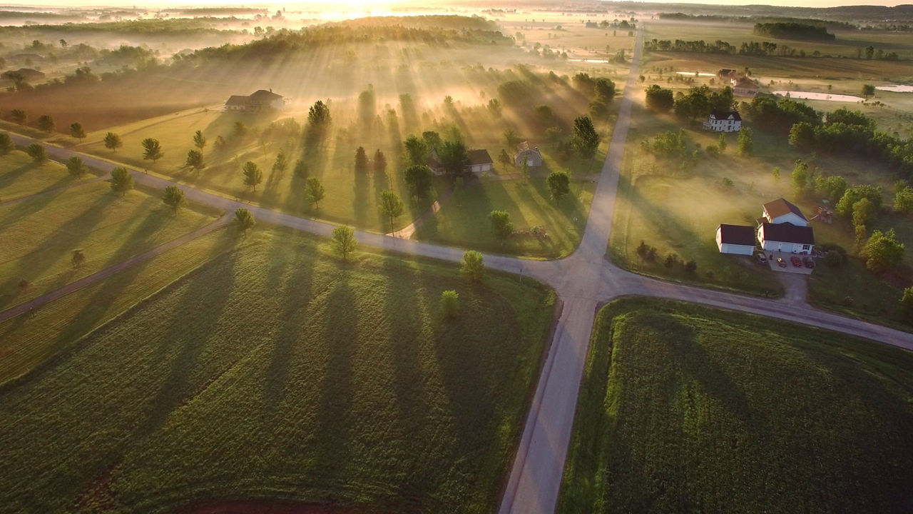 Straßenkreuzung umgeben von grünen Feldern bei Sonnenaufgang