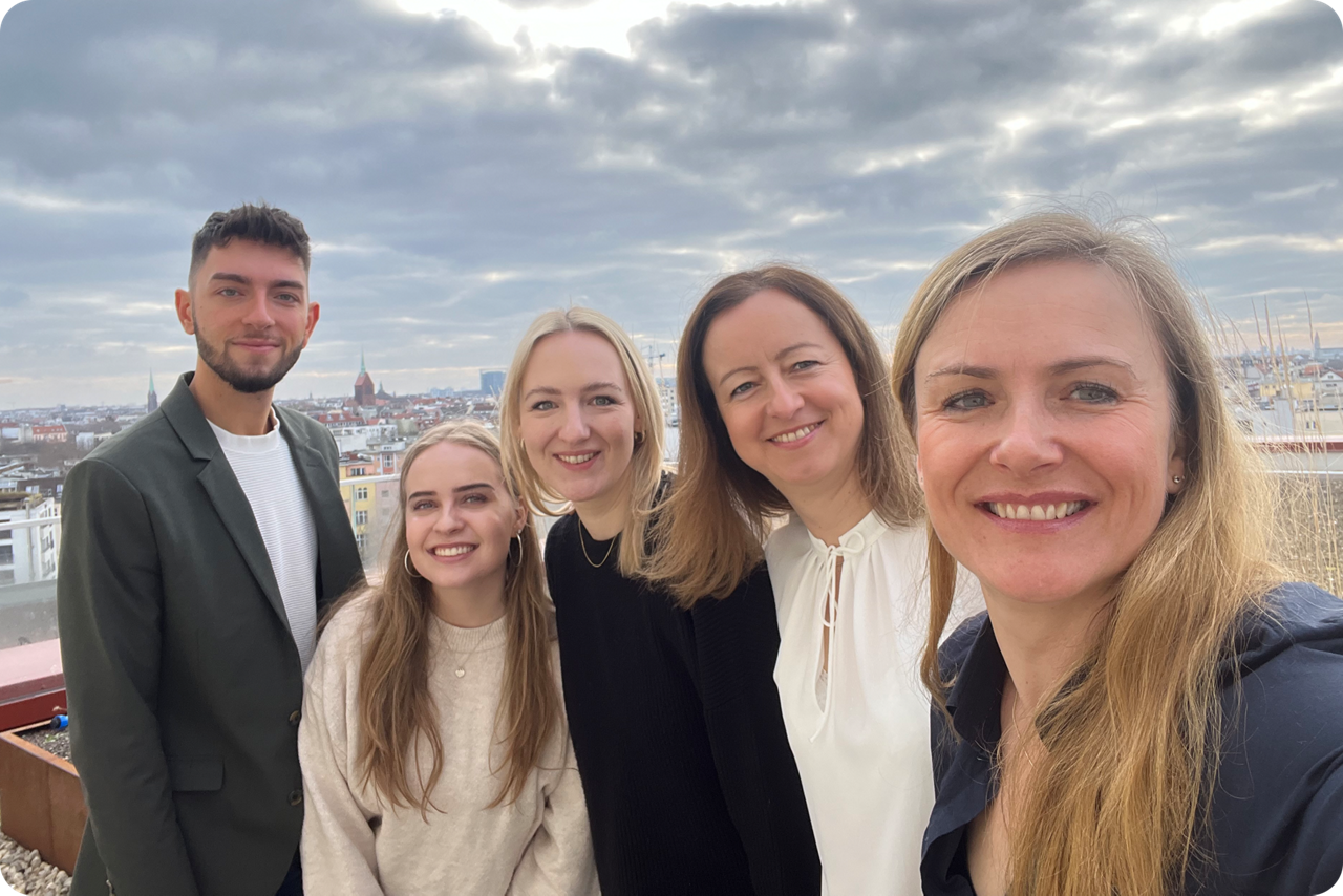 Vier Frauen und ein Mann stehen auf einer Terasse und lächeln für ein Selfie in die Kamera, im Hintergrund ist Berlin zu sehe